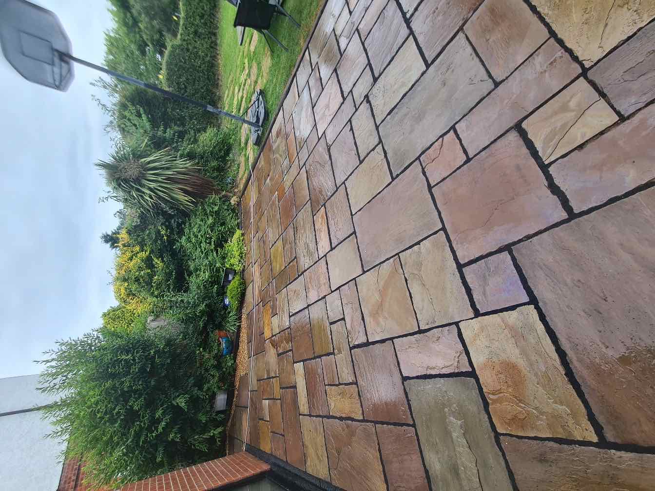 Multi-coloured Indian sandstone patio bordered by mature planting